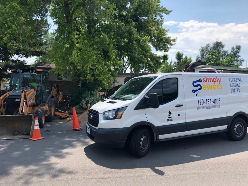 A Simply Sewers van parked on a residential street next to an excavator and traffic cones, under a tree.