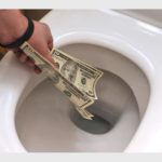 Person tossing 10-dollar bills into a white toilet bowl
