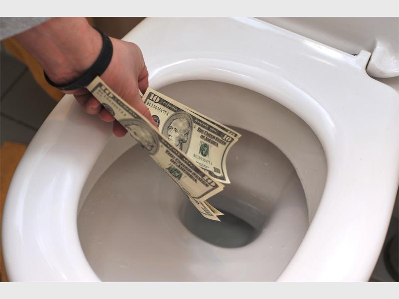 Person tossing 10 dollar bills into a white toilet bowl