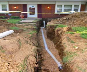 A residential sewer line replacement under construction with a trench dug through the yard and new sewer pipe being installed.