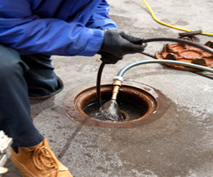 A technician kneels on the ground to snake out a clogged outdoor drain.