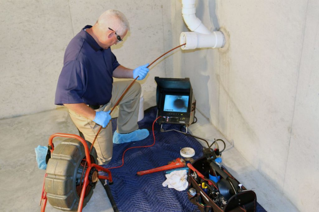 man inspecting a pipe mounted on the wall with sewer camera