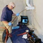 man inspecting a pipe mounted on the wall with sewer camera