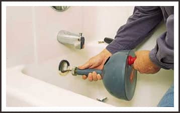 A repairman using a drain snake to clear a clogged bathtub drain