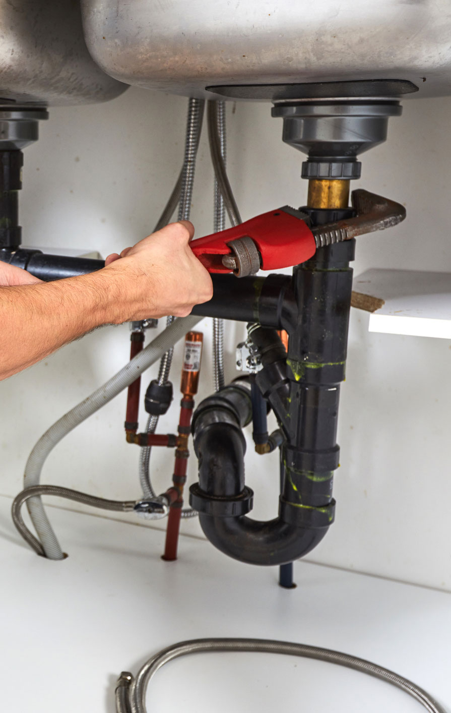 A plumber fixes pipes under a kitchen sink using pump pliers