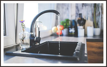 A tall kitchen faucet with water running from the tap.