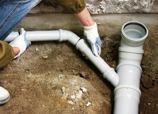 Man in gloves in a hole repairing a sewer line pipe