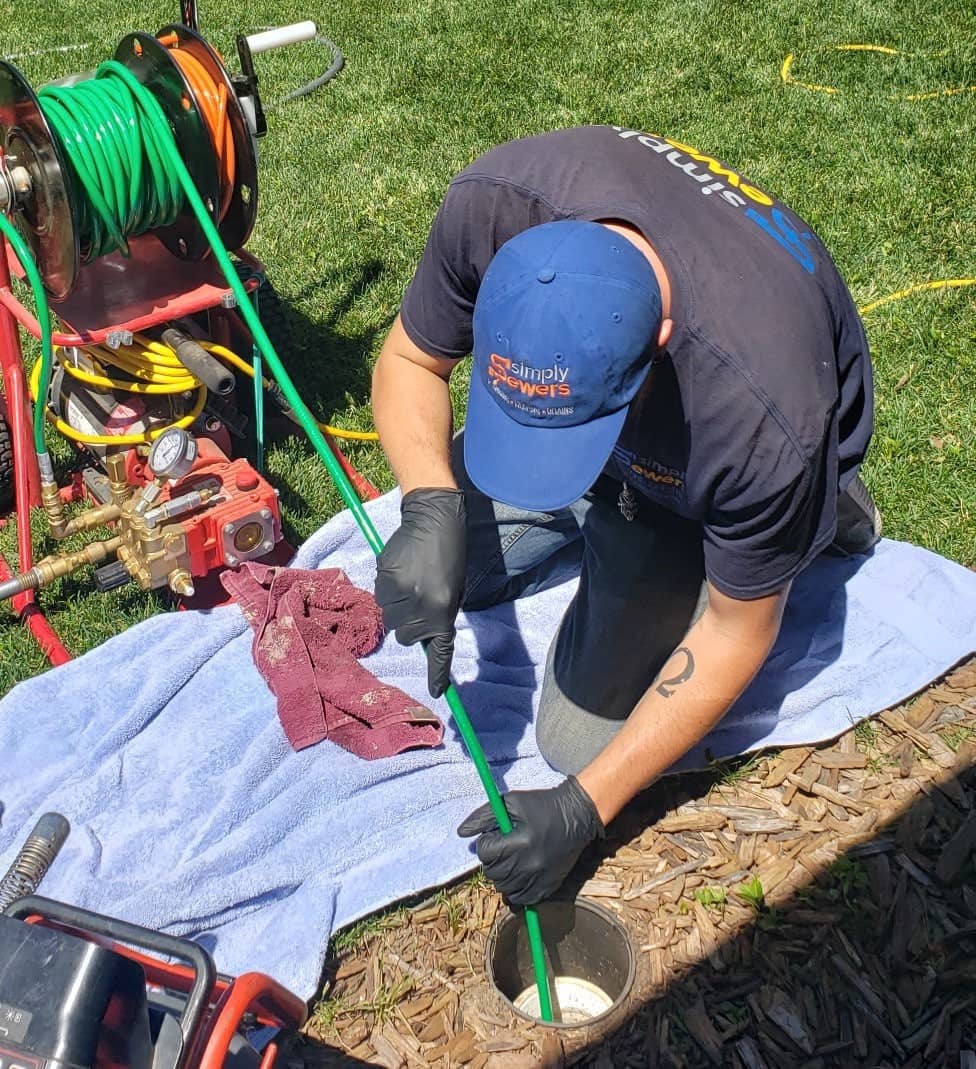 A plumbing technician is performing a sewer cleanout from an outside access port.