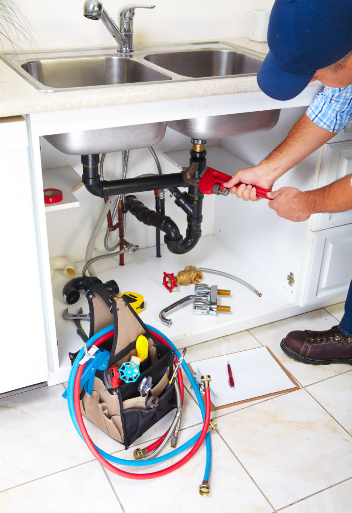 A plumber in fixes pipes under a kitchen sink.