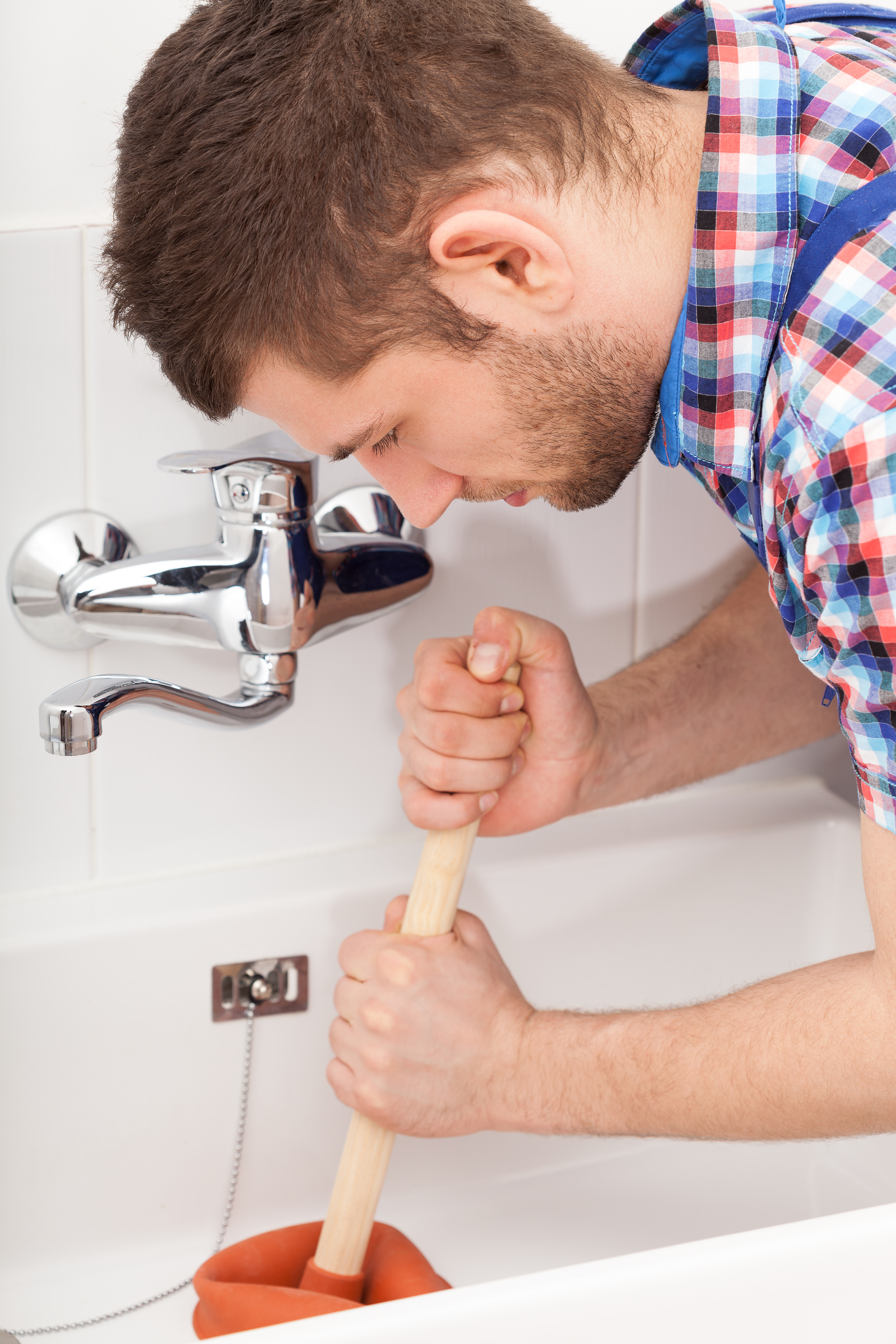 Young plumber unclogging a bathtube drain with plunger