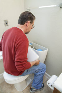 A man looks at a toilet tank to find a leak.