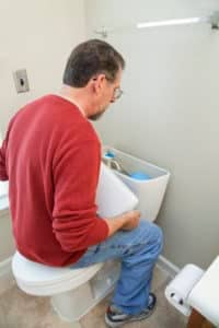 A man looks at a toilet tank to find a leak.