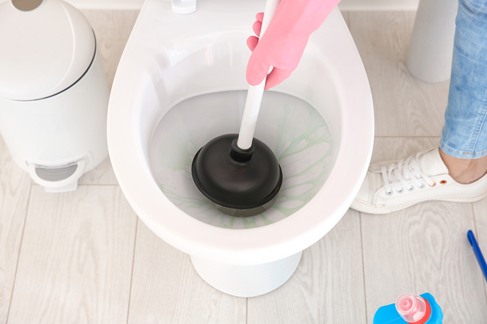 A woman works with a black plunger to fix a clogged toilet