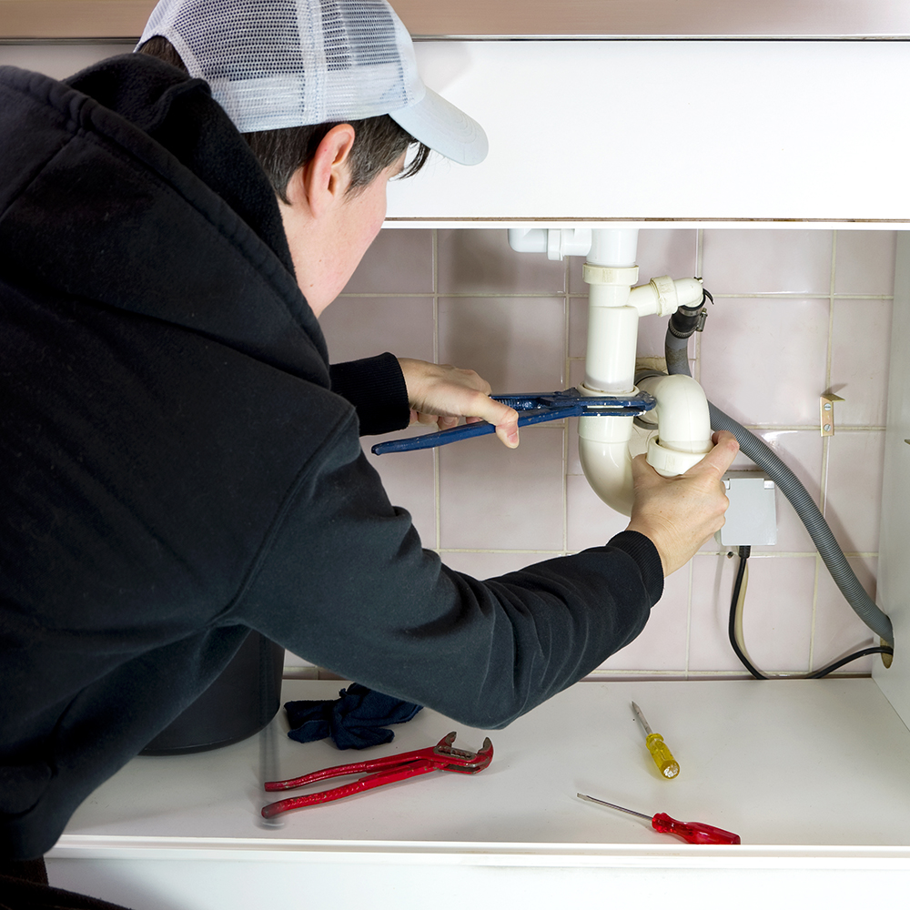 A plumber works with a wrench to repair a pipe under a kitchen sink