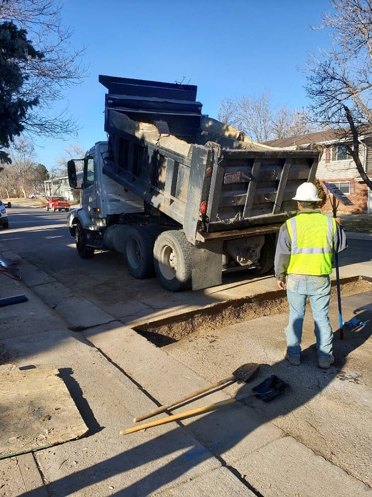 A gravel truck is dumping dirt back into a trench where Simply Sewers replace the sewer line for a Golden, CO home