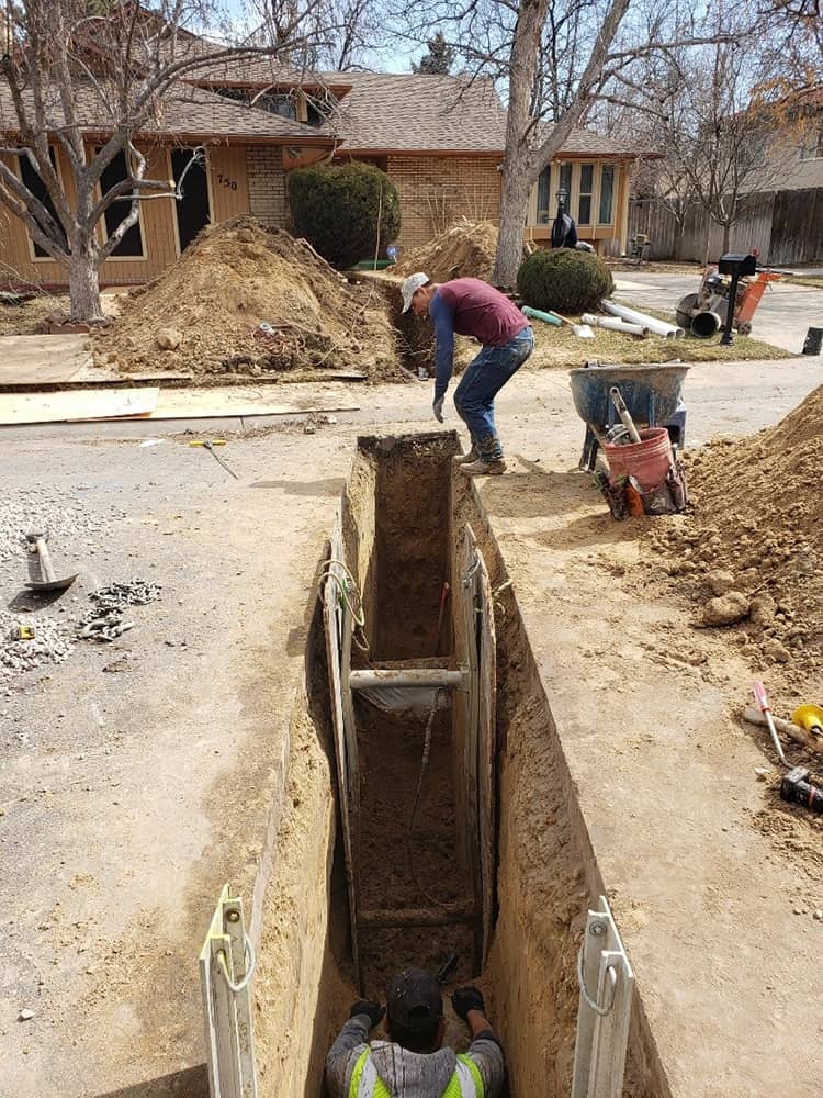 men working on a water line excavation in front of a house