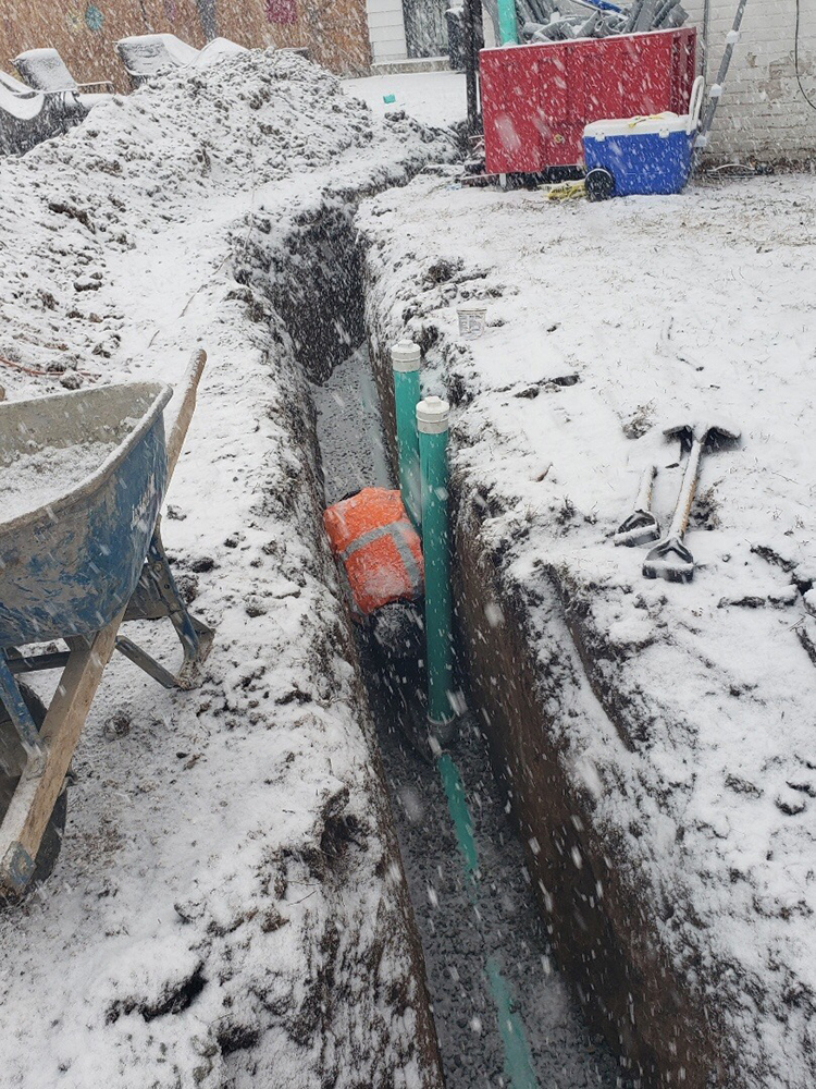 A Simply Sewers technician is working in a trench in the backyard of a Centennial, CO home to replace a sewer line in the snow
