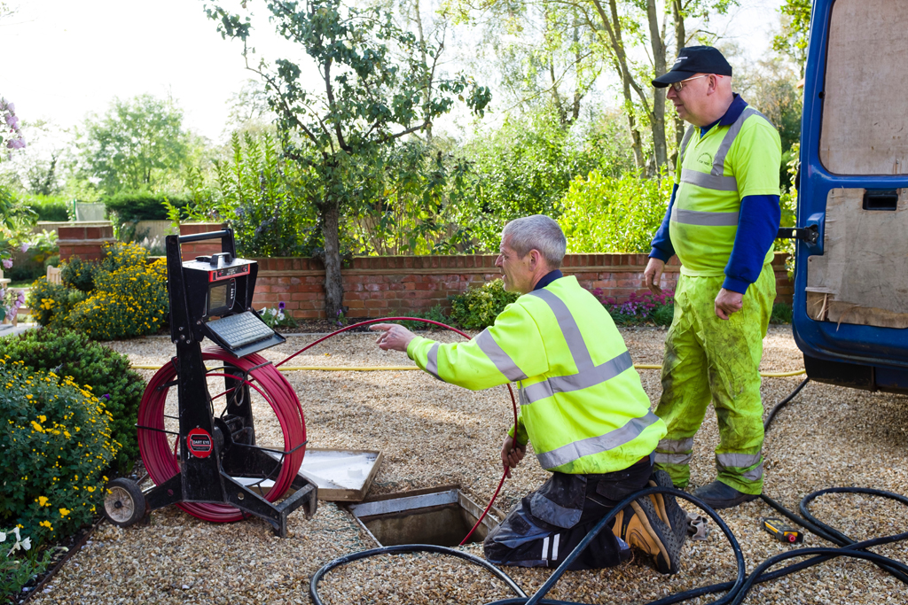 Two men in reflective safety wear inserting sewer camera into a residential system