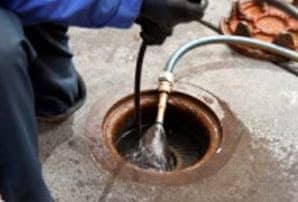 A littleton plumber is accessing an outdoor sewer drain and cleaning it with a drain auger and water.