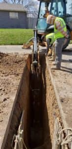 A backhoe digs a whole in the street to replace a broken sewer line