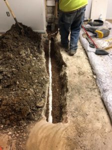 A sewer line is being replaced in a basement floor.